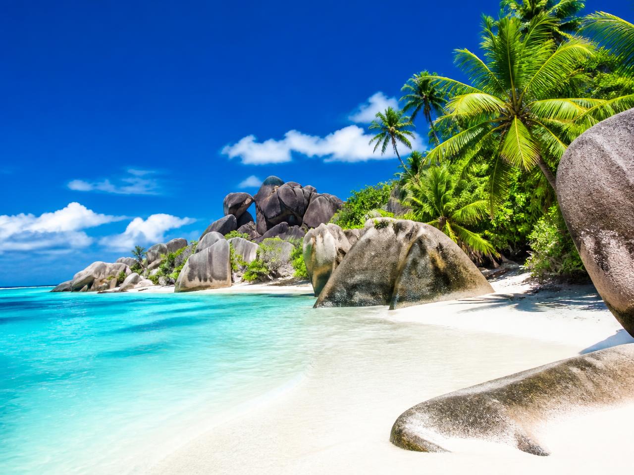 Granite boulders on a white Seychelles beach beside clear water