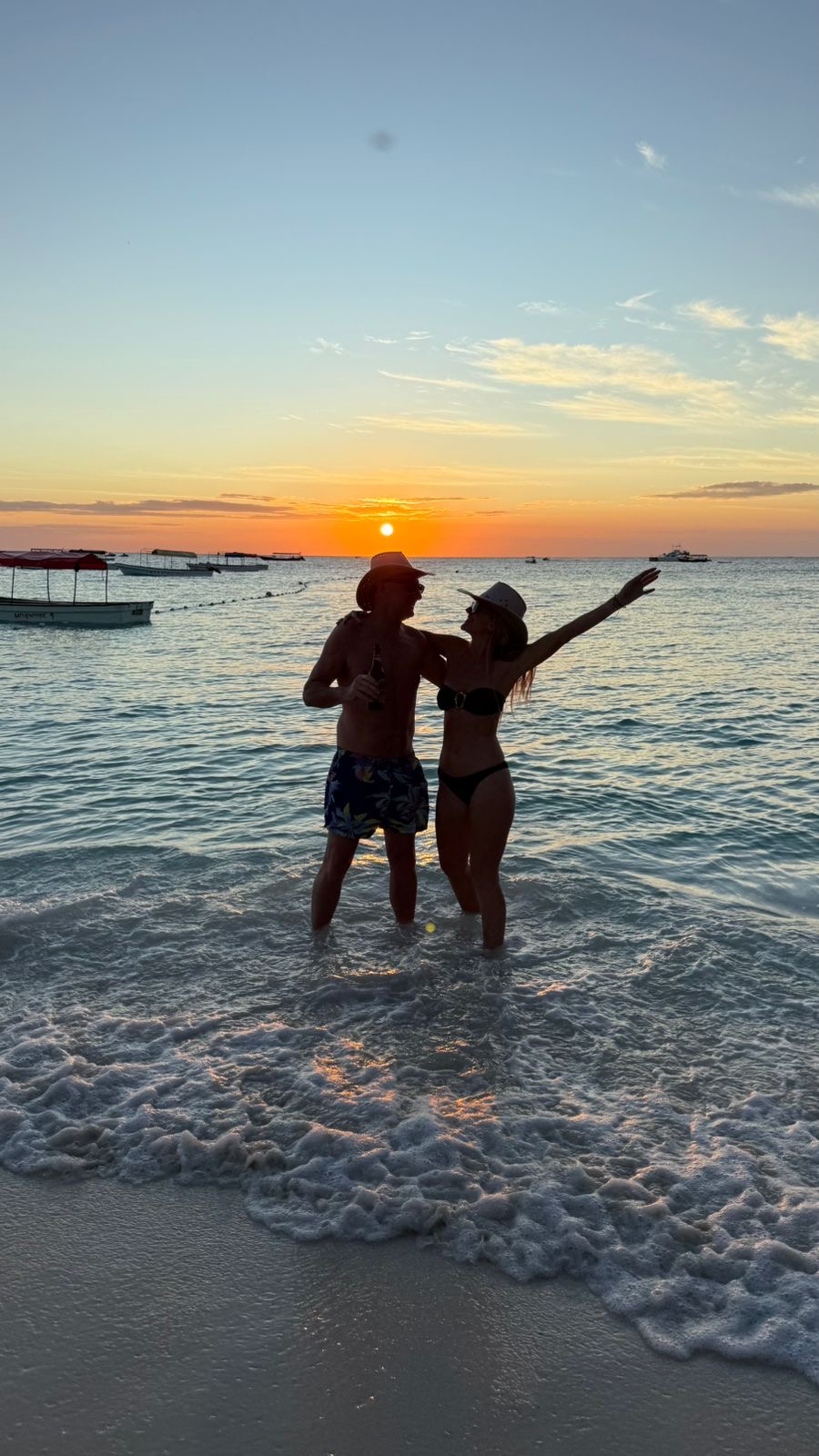 A couple stands in the warm shallows of a Zanzibar beach at sunset